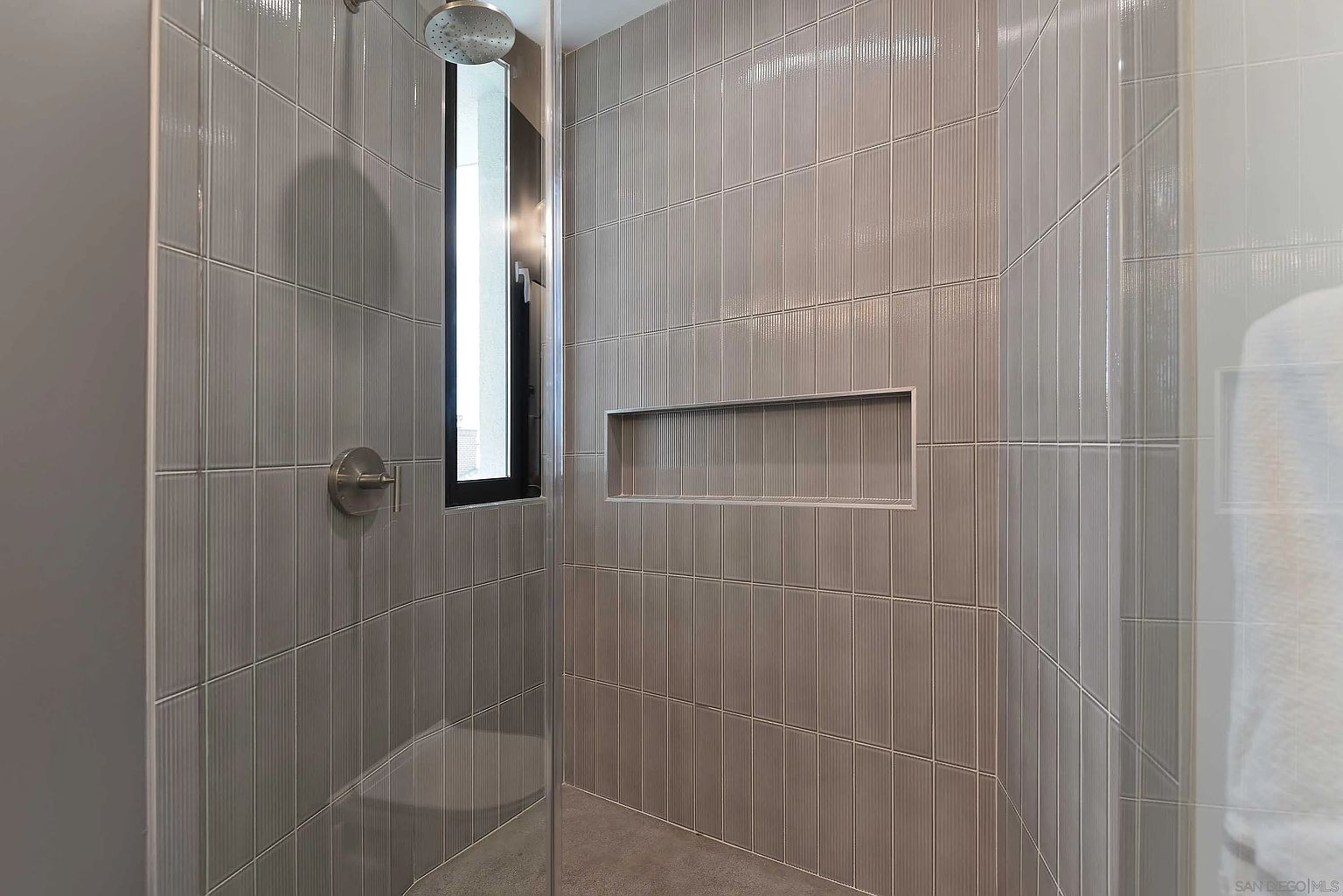 This is a modern bathroom featuring gray vertical tiles, a built-in niche, and a glass shower enclosure. The shower has a rainfall showerhead and a sleek, minimalist design. The overall impression is clean and contemporary, with a focus on functionality and style.