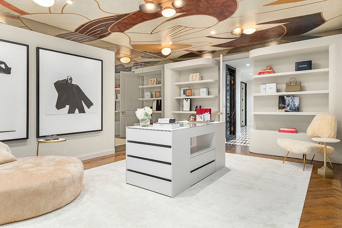 This is a luxurious walk-in closet featuring custom shelving, a central island with drawers, and a plush seating area. The ceiling is adorned with a unique floral design and recessed lighting. The space is well-organized and exudes a high-end, sophisticated aesthetic, perfect for showcasing a curated wardrobe.