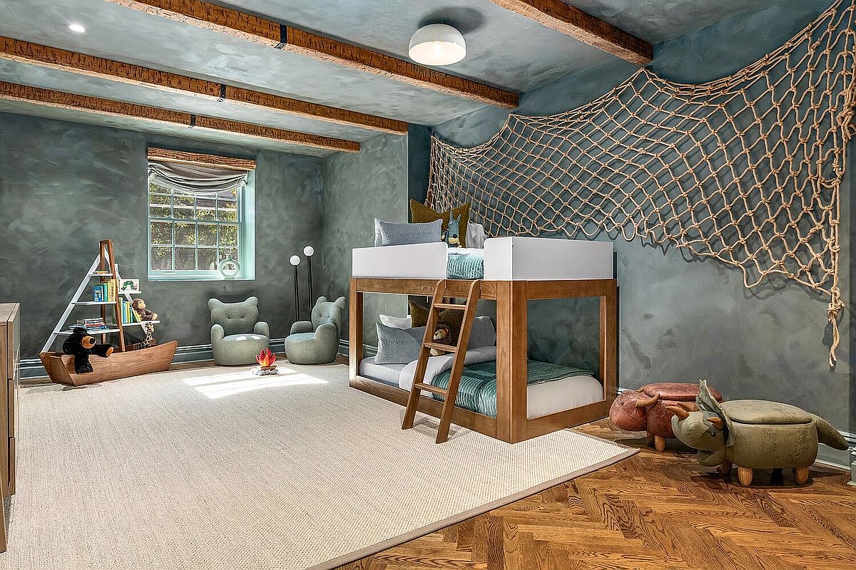 This is a charming children's bedroom featuring a custom-built bunk bed with a wooden frame and white accents. The room is decorated with a nautical theme, including a fishing net on the wall and playful animal-shaped ottomans. The walls are painted in a textured blue-gray, complemented by exposed wooden beams on the ceiling, creating a cozy and imaginative space.
