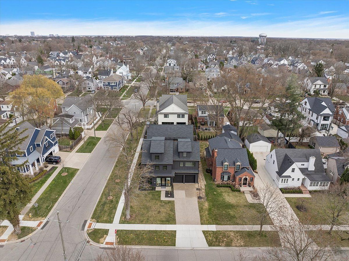 This aerial view showcases a charming residential neighborhood with well-maintained homes and mature trees. The houses feature a mix of architectural styles, with neatly manicured lawns and paved driveways. The perspective gives a comprehensive overview of the property's setting within the community, highlighting its proximity to other homes and the overall neighborhood layout.