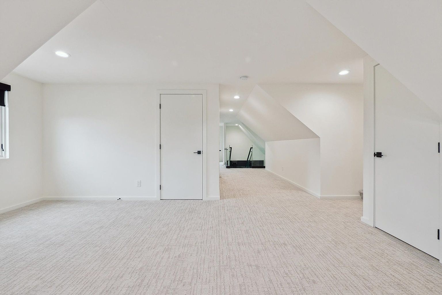 The image showcases a bright, minimalist hallway with white walls and light-colored carpet. The hallway features multiple doorways and recessed lighting, creating a clean and spacious feel. The design emphasizes simplicity and functionality, making it an appealing transitional space within the home.