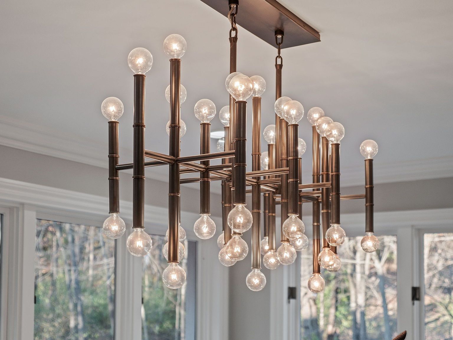 The image showcases a modern chandelier with multiple exposed bulb lights. The fixture features a bronze-colored metal frame with a geometric design, creating a contemporary and stylish focal point. The lighting fixture is suspended from the ceiling, adding an elegant touch to the space.