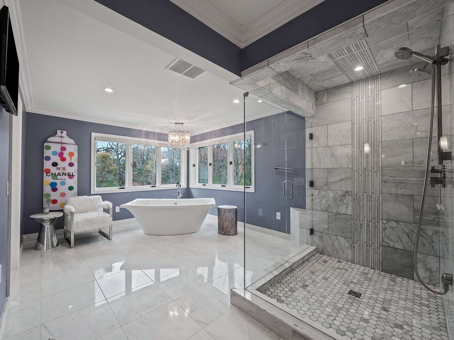 This is a luxurious primary bathroom featuring a freestanding soaking tub positioned beneath a bay of windows, offering natural light and views. A spacious walk-in shower with glass enclosure showcases elegant tile work and modern fixtures. The room is finished with high-end materials and a sophisticated color palette, creating a spa-like atmosphere.