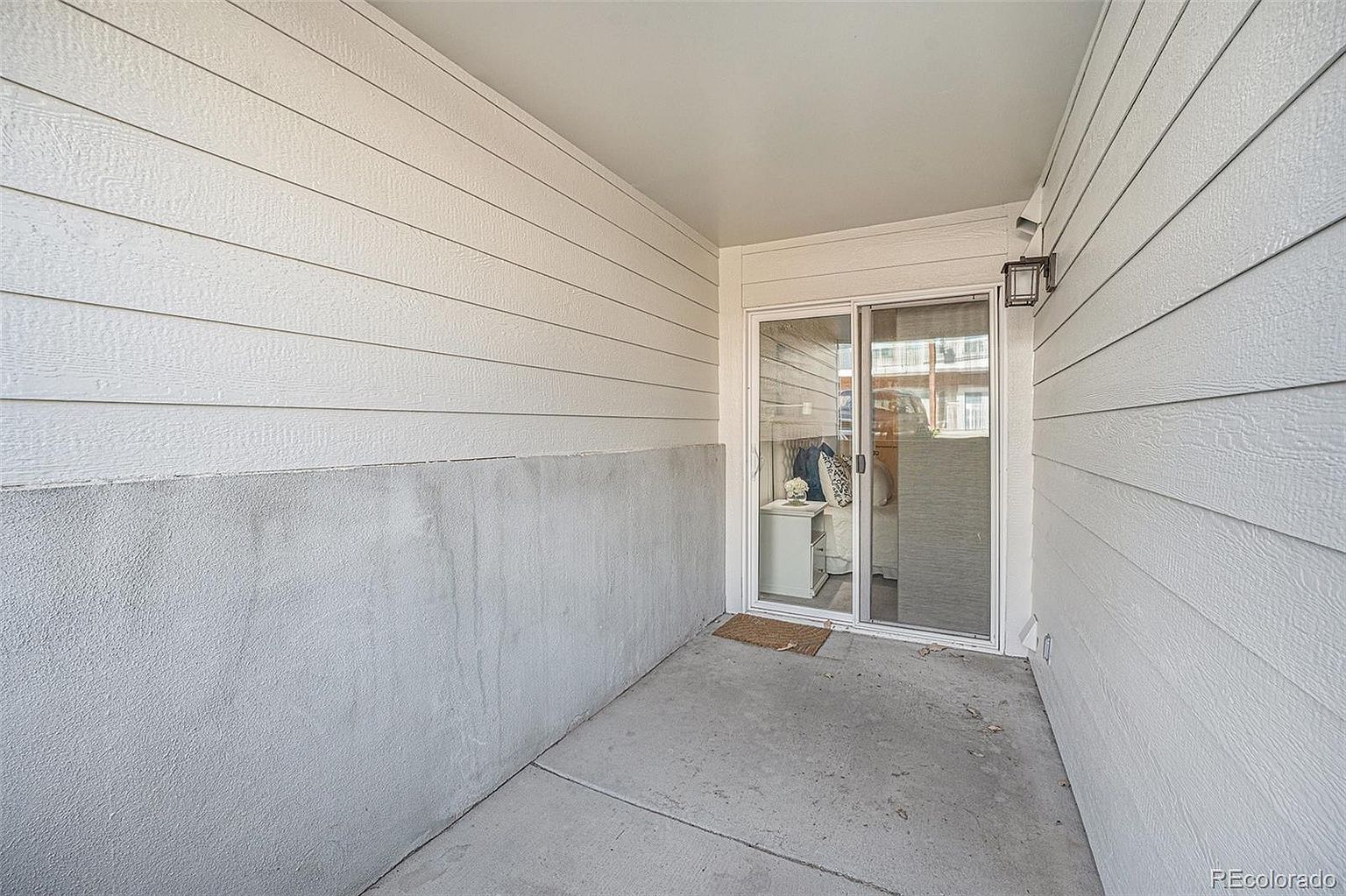 This image showcases a well-maintained outdoor patio or balcony area. The space features a concrete floor, light-colored siding, and a sliding glass door leading indoors. The area appears clean and inviting, offering a private outdoor space for relaxation or entertainment.