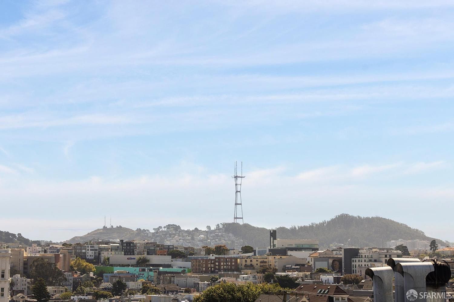 This aerial view showcases a cityscape with a prominent tower in the distance, set against a backdrop of rolling hills and a clear blue sky. The urban landscape features a mix of residential and commercial buildings, offering a sense of community and accessibility. The overall impression is one of a vibrant city with natural beauty in the surrounding environment.