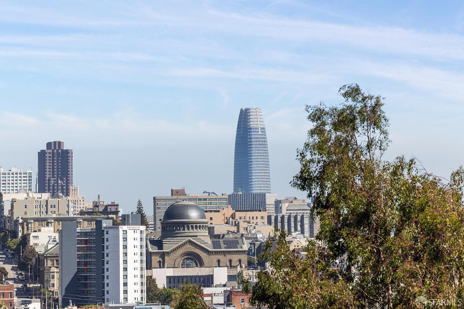 This image showcases a cityscape featuring a mix of architectural styles, including modern skyscrapers and traditional buildings with a domed structure. The prominent skyscraper in the background adds a sense of urban grandeur, while the surrounding buildings create a diverse and interesting skyline. The presence of trees in the foreground adds a touch of nature to the urban environment.