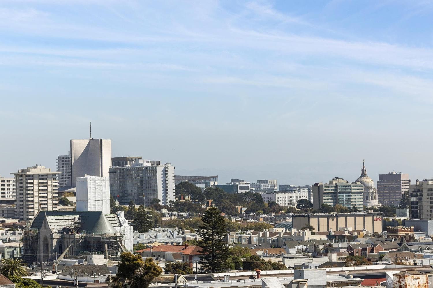 This aerial view showcases a cityscape with a mix of residential and commercial buildings under a clear sky. The architecture varies from modern high-rises to traditional houses, creating a diverse urban landscape. The image provides a sense of the city's scale and density, highlighting its vibrant and dynamic environment.