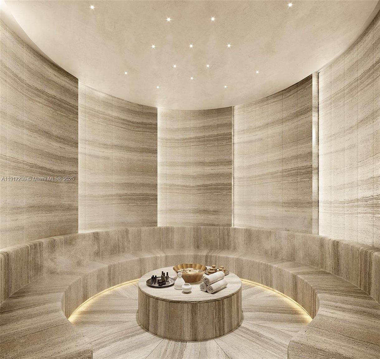 This luxurious spa or steam room features a circular layout with curved stone-clad seating integrated into the walls. The space is illuminated by recessed ceiling lights and soft under-bench lighting, creating a serene and high-end atmosphere. A central circular stone table holds spa accessories, emphasizing a tranquil, wellness-focused environment.
