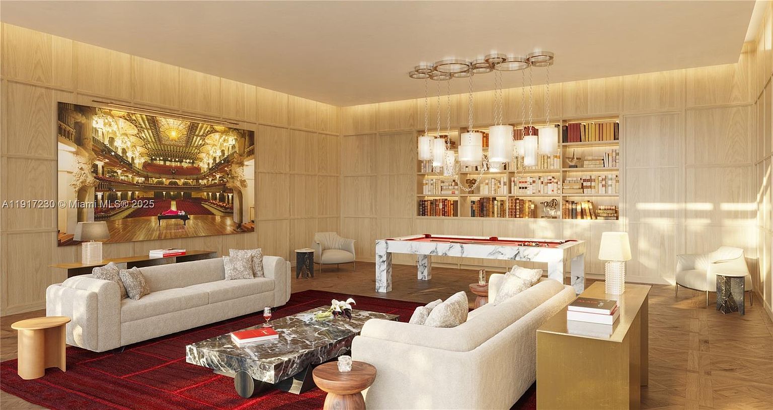 This sophisticated living room features light wood-paneled walls and a large, vibrant art piece depicting an ornate theater interior. The space is furnished with two plush, light-colored sofas arranged around a low, stone-topped coffee table, with a white stone-base pool table positioned near a built-in bookshelf. A deep red area rug anchors the seating area, while a series of modern, cylindrical pendant lights hangs from the ceiling, creating an elegant and refined atmosphere.
