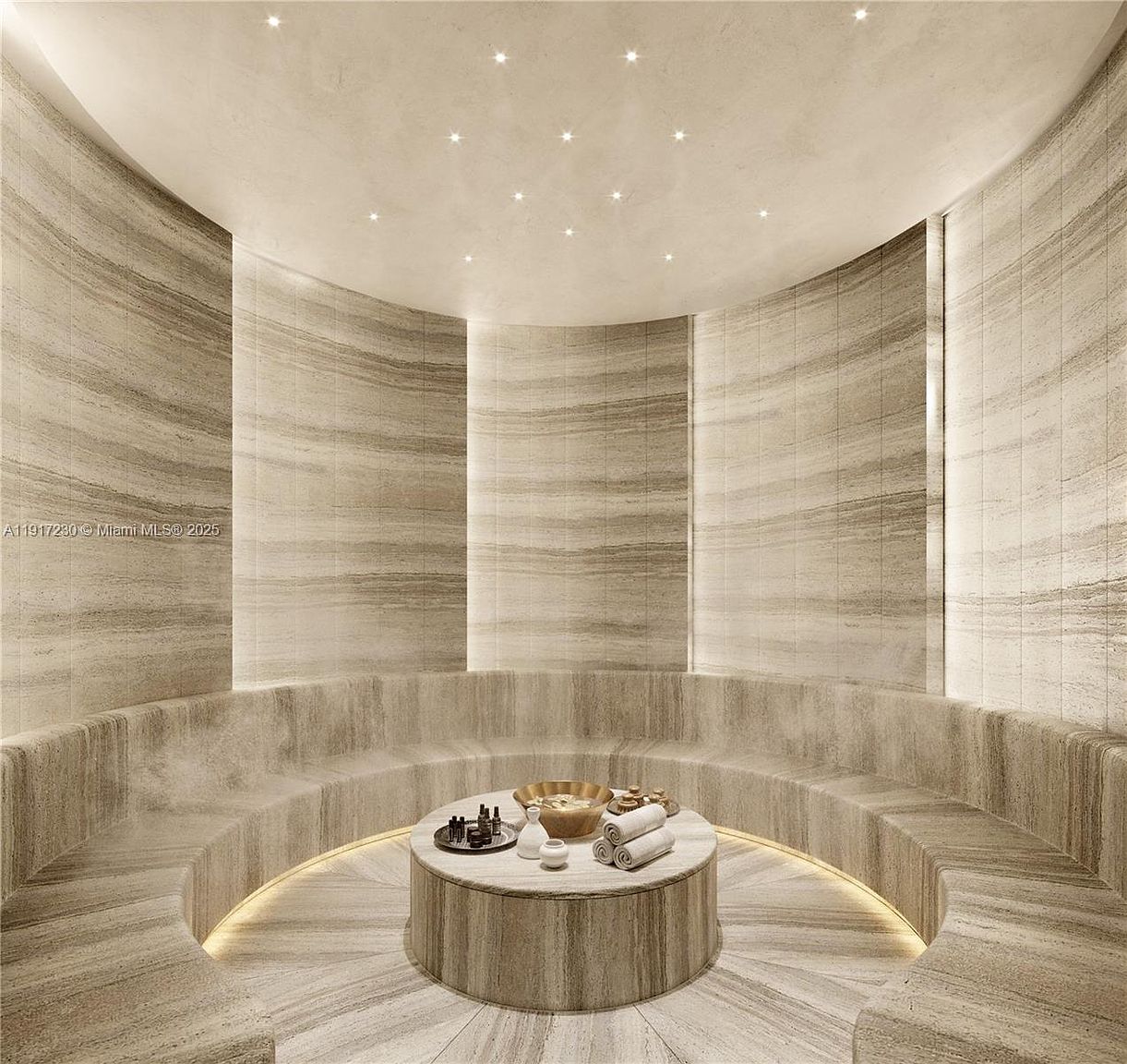 This image showcases a luxurious, circular steam room or spa facility characterized by curved, stone-clad walls and integrated ambient lighting. A central circular stone platform serves as a focal point, holding a decorative metal bowl and rolled towels, while recessed lighting in the ceiling mimics a starry night sky. The space conveys a high-end, tranquil atmosphere designed for relaxation and wellness.