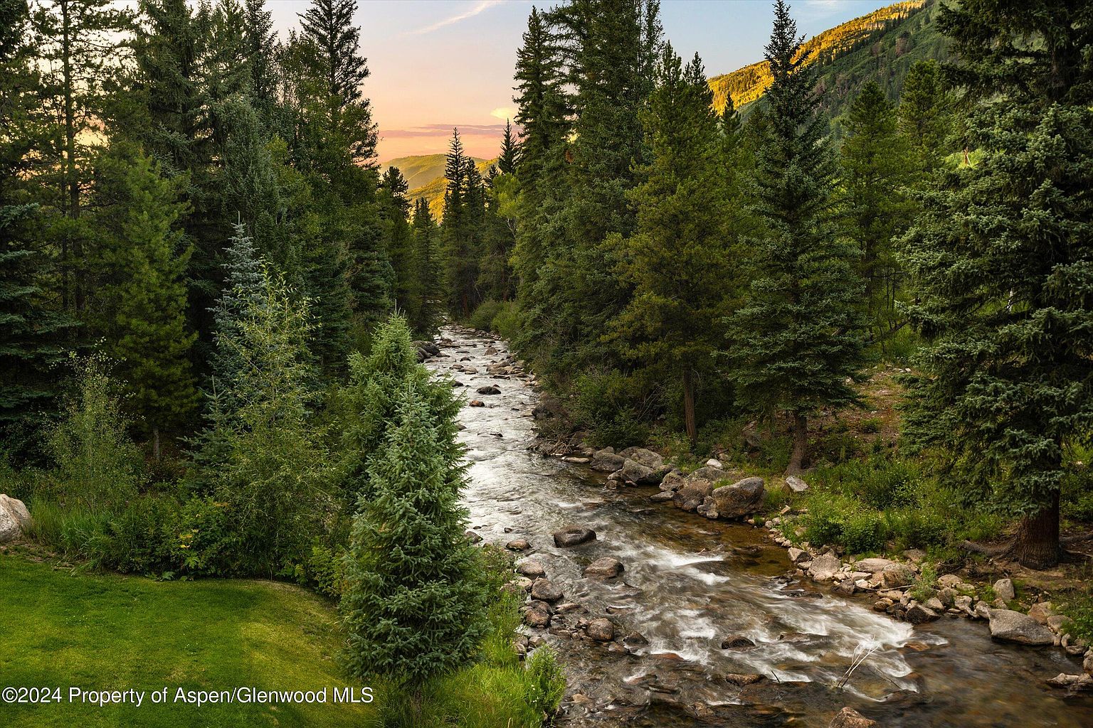 This picturesque outdoor scene showcases a serene river flowing through a lush, green forest. The landscape features a mix of evergreen trees and natural vegetation, creating a tranquil and inviting atmosphere. The image captures the beauty of nature, suggesting a peaceful and private setting for a property.