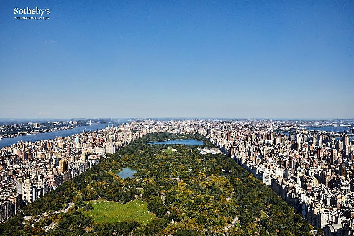This stunning high-altitude aerial view captures the iconic expanse of Central Park in New York City, flanked by dense urban skyscrapers on both sides. The perspective highlights the lush greenery of the park contrasting with the surrounding concrete jungle, with the Hudson River and the George Washington Bridge visible in the distance. It provides a grand, cinematic sense of scale and prime location, emphasizing the prestige of the surrounding real estate.