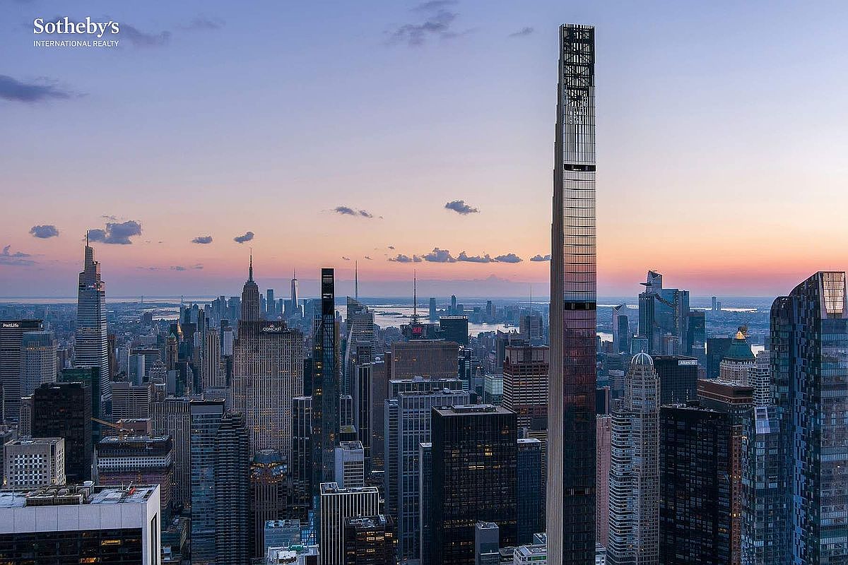 This high-altitude aerial view captures the iconic New York City skyline at dusk, dominated by the striking, slender silhouette of 111 West 57th Street. The composition highlights the dense urban landscape, featuring a mix of historic and modern skyscrapers bathed in the soft, warm glow of the setting sun. The perspective provides a dramatic sense of scale and luxury, emphasizing the building's prominent position within the city's architectural tapestry.
