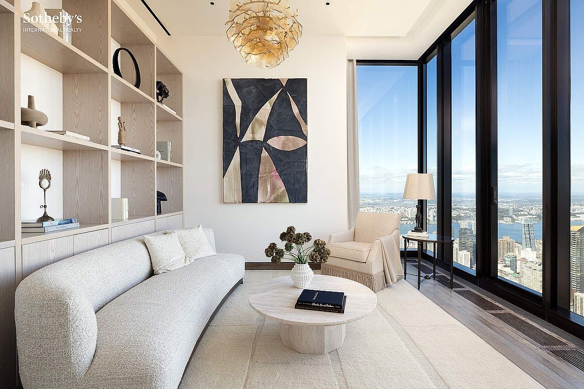 This sophisticated, high-rise living room features a minimalist, contemporary aesthetic with a neutral color palette and floor-to-ceiling windows offering expansive city views. The space is furnished with a textured, curved sofa, a round stone coffee table, and a plush armchair, all anchored by a large abstract painting and custom built-in shelving. The cinematic perspective captures the seamless blend of luxury interior design and the dramatic urban backdrop.
