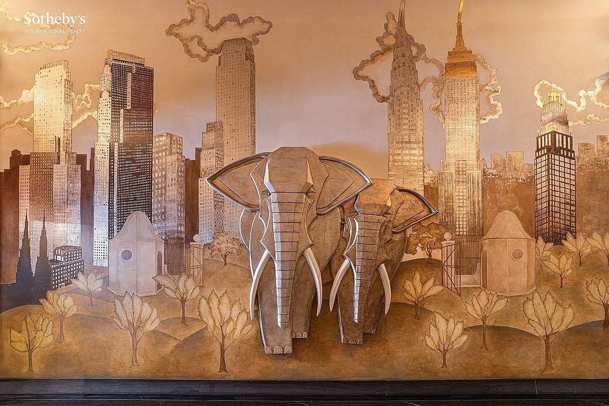 This image showcases a large, artistic mural featuring two prominent, sculpted elephants set against a stylized, monochromatic cityscape of New York City. The artwork utilizes a warm, sepia-toned palette with intricate textures that blend the natural forms of the animals with iconic skyscrapers like the Chrysler and Empire State Buildings. The perspective is head-on and cinematic, highlighting the mural as a sophisticated, high-end decorative feature that adds a unique, artistic focal point to the interior space.