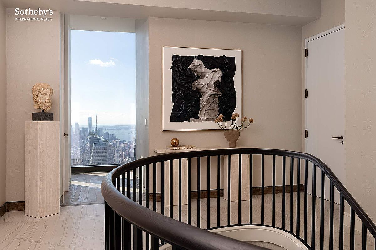 This sophisticated landing area features a curved staircase with a dark wood railing, leading the eye toward a stunning floor-to-ceiling window that frames a panoramic city skyline. The space is elegantly appointed with a minimalist console table, a sculptural bust on a pedestal, and a striking abstract art piece, creating a refined and artistic atmosphere. The neutral color palette and clean lines emphasize the luxury and high-end design of this modern residence.