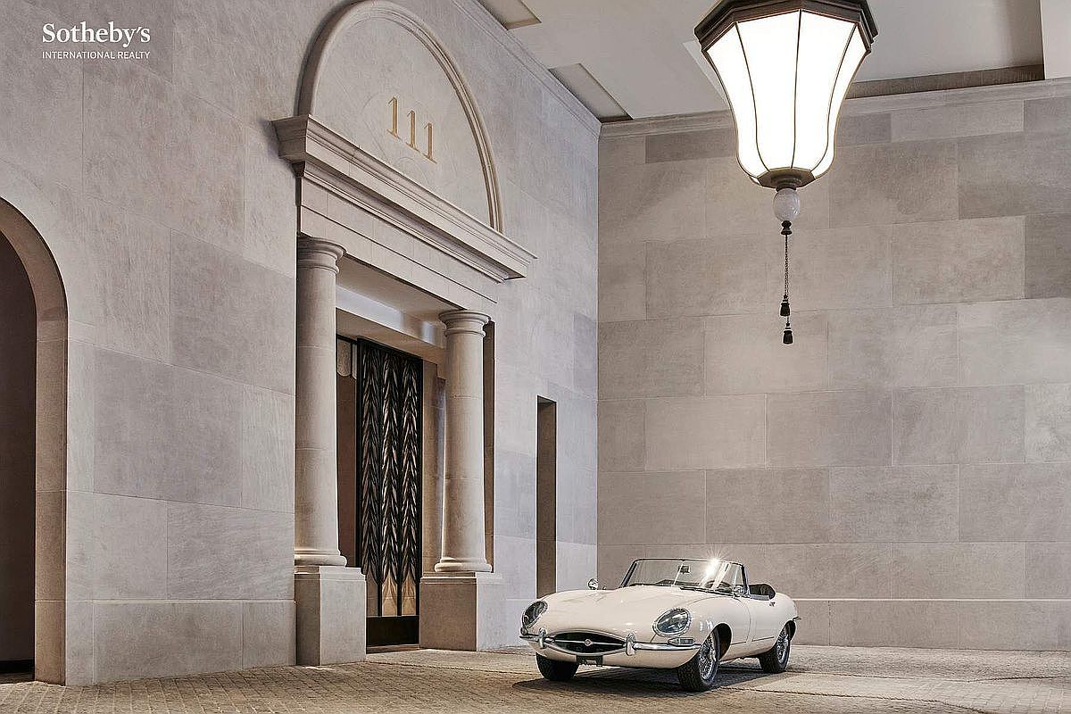 This sophisticated porte-cochère features a grand, stone-clad entryway marked by the number 111, accented by classical columns and an elegant arched pediment. A vintage white convertible is parked prominently in the foreground, enhancing the luxurious and exclusive atmosphere of the arrival court. The scene is illuminated by a large, ornate hanging lantern, creating a cinematic and high-end impression suitable for a prestigious residential property.