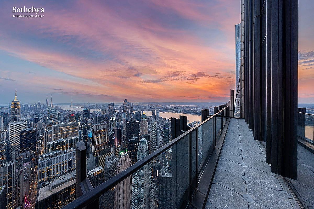 This high-altitude balcony offers a breathtaking, panoramic view of the New York City skyline at sunset, featuring iconic landmarks like the Empire State Building. The space is finished with modern, hexagonal stone tiling and a sleek glass railing that maximizes the dramatic urban vista. The perspective is cinematic, capturing the vast scale of the city from a luxurious, elevated vantage point.
