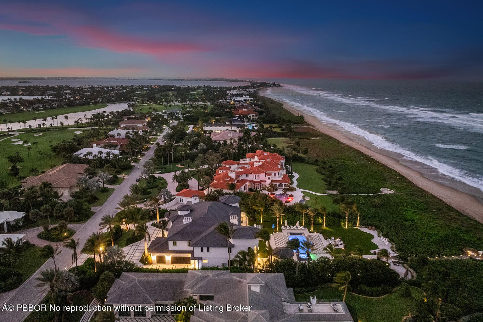 This aerial view showcases a luxurious coastal estate with multiple buildings, a swimming pool, and meticulously landscaped grounds. The property is situated along a pristine beach, with a golf course visible in the distance. The overall impression is one of opulence and exclusivity, highlighting the prime location and high-end amenities.