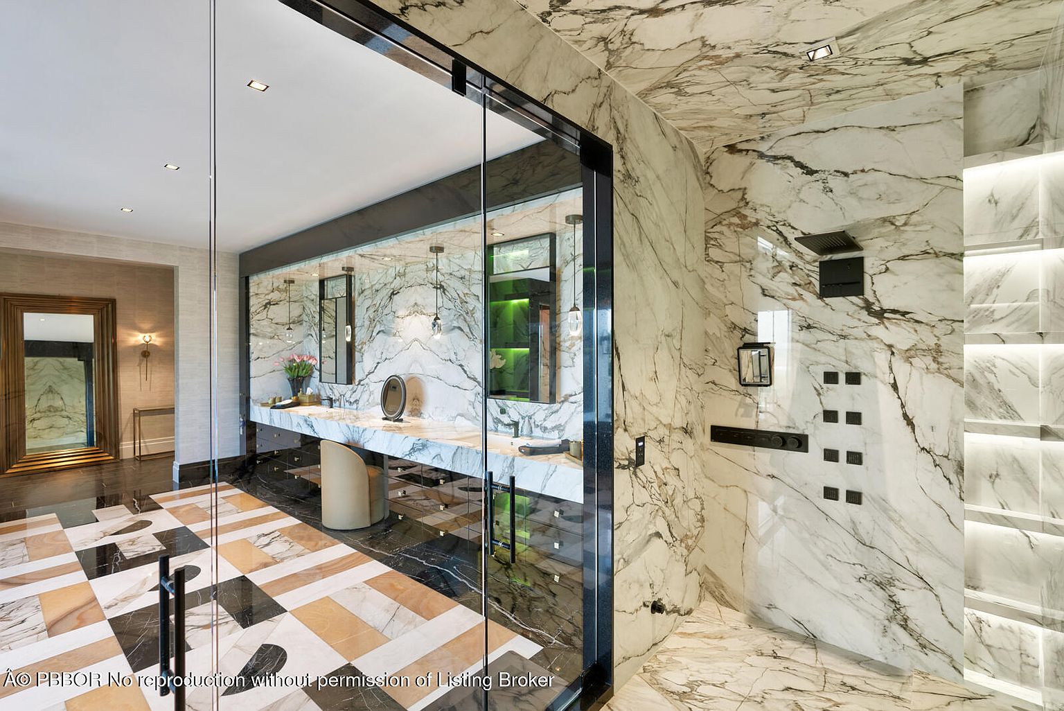 This is a luxurious primary bathroom featuring marble walls and flooring with a unique geometric pattern. The bathroom includes a glass-enclosed shower with multiple showerheads and body jets, as well as a vanity area with dual sinks and modern fixtures. The overall impression is one of opulence and high-end design.