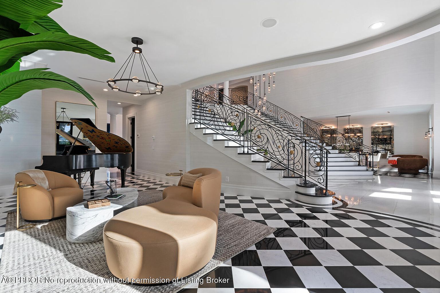This grand foyer features a striking black and white checkered marble floor, a curved staircase with ornate wrought iron railings, and a modern chandelier. A grand piano sits to the left, complemented by stylish seating and a large plant, creating a luxurious and inviting entrance. The space is bright and airy, showcasing the home's elegant design and high-end finishes.