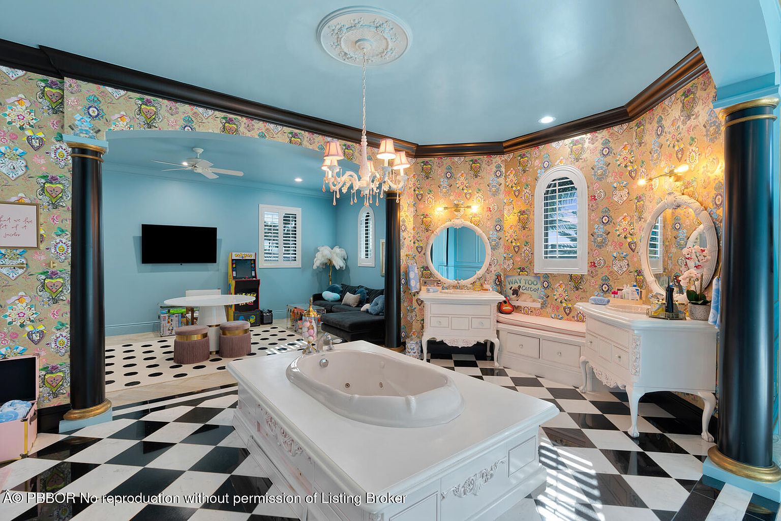 This opulent primary bathroom features a unique design with a black and white checkered floor, a large white jacuzzi tub, and dual vanities with round mirrors. The walls are adorned with patterned wallpaper, and the ceiling is painted a light blue, creating a whimsical and luxurious atmosphere. A separate blue-walled area includes a TV and seating, adding a playful touch.