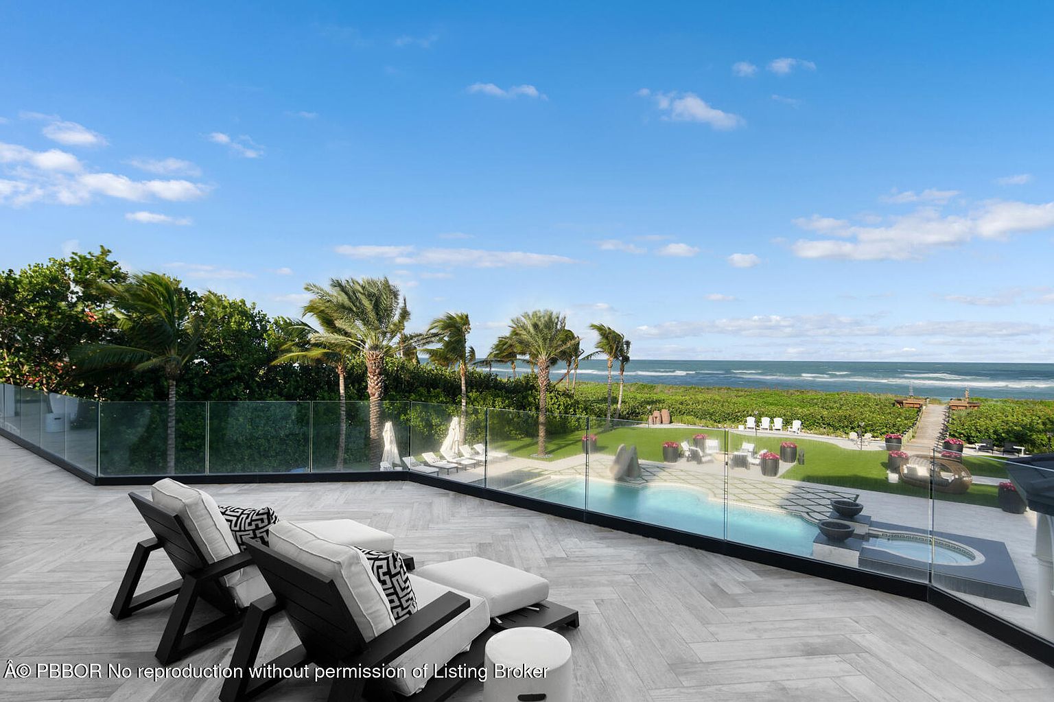 This image showcases a luxurious patio or balcony with a stunning ocean view. The space features modern lounge chairs, a glass railing for unobstructed views, and a well-maintained pool and spa area. Lush greenery and palm trees add to the tropical ambiance, creating an inviting outdoor living space.