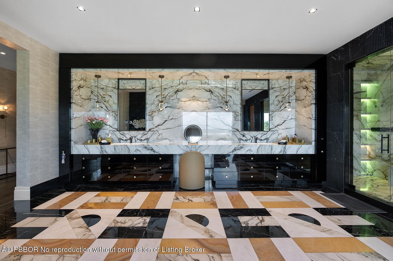 This is a luxurious primary bathroom featuring a double vanity with marble countertops and backsplash, black cabinetry, and modern fixtures. The floor is a patterned mix of marble and other stone, adding a unique design element. A round mirror sits between the two vanities, and a glass-enclosed shower is visible on the right.
