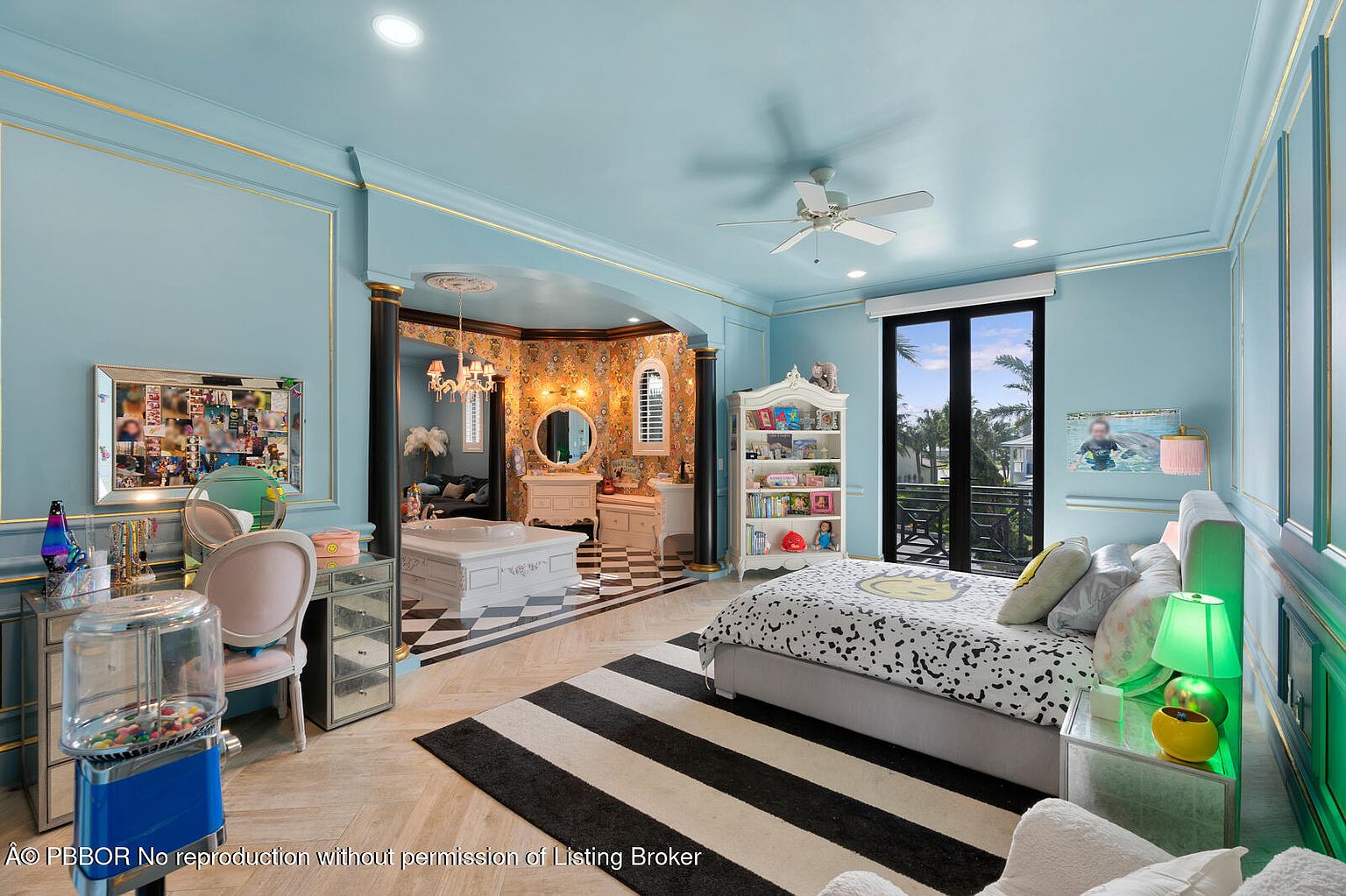 This is a whimsical and uniquely designed bedroom featuring a light blue color scheme with gold trim. The room includes a sleeping area with a patterned bed, a vanity area with a mirrored desk, and an adjacent bathroom area with a tub and patterned wallpaper. The overall impression is playful and luxurious.