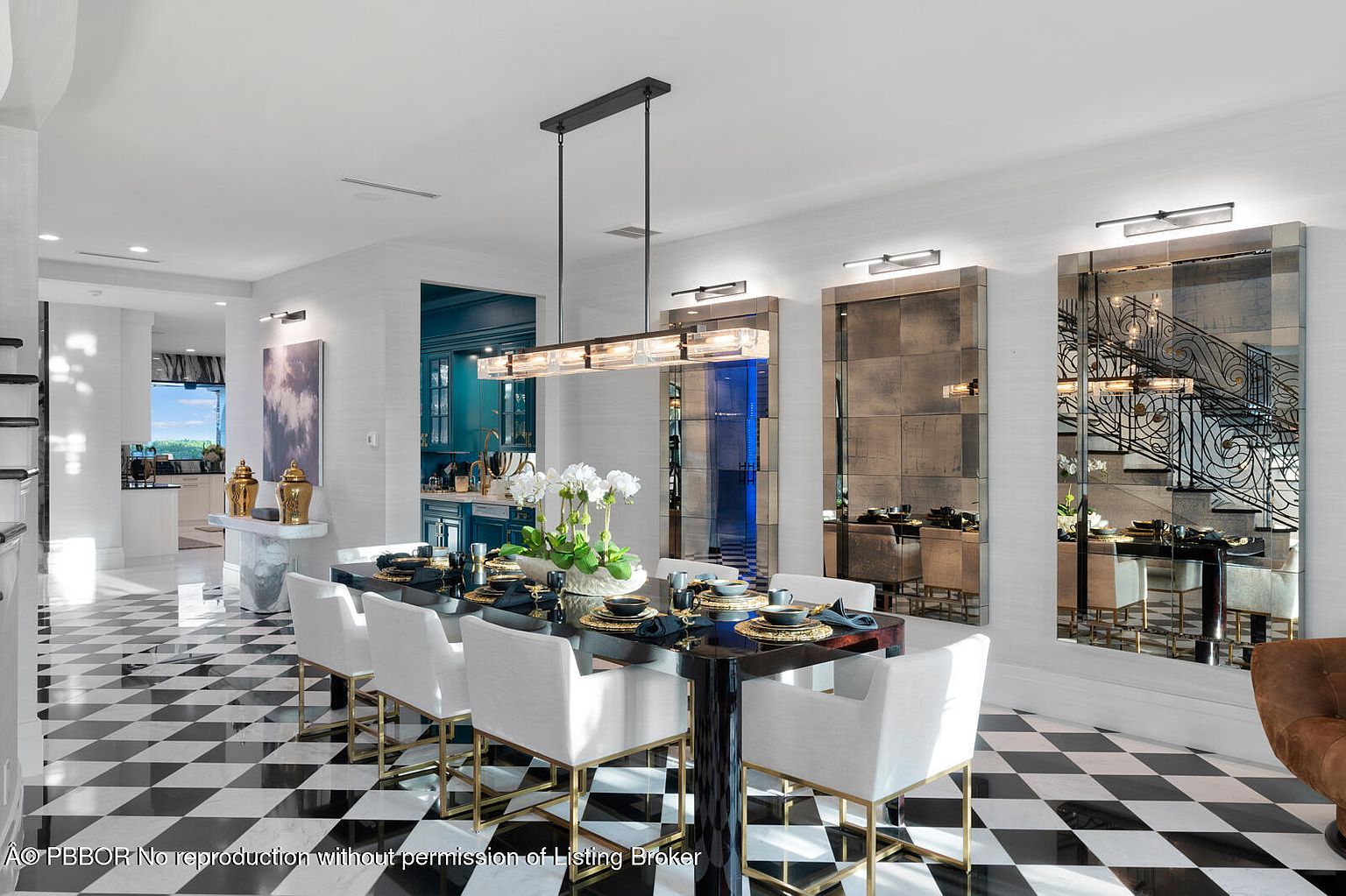 This interior shot showcases a luxurious dining room with a black and gold dining table set for a formal meal, surrounded by white upholstered chairs with gold accents. The room features a striking black and white checkered floor, mirrored wall panels, and a modern linear chandelier, creating an elegant and sophisticated ambiance.
