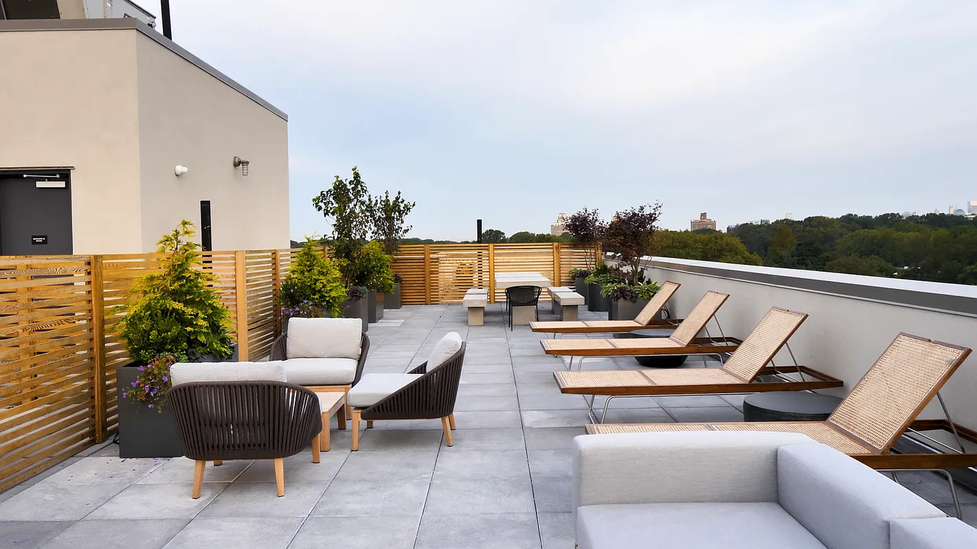 This is a rooftop patio or deck that appears to be part of an apartment building or condominium complex. The space is set up with lounge chairs, seating arrangements, and planters for decorative greenery. It gives the impression of an exclusive, well-maintained outdoor living area.