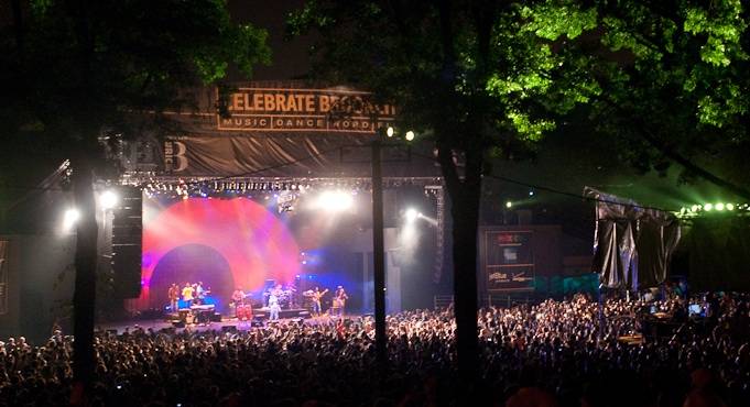 This image depicts an outdoor concert venue at night, filled with a large crowd. The stage is set up with lighting and performers, visible beneath a banner. This indicates an amenity or event space within a community, adding to its appeal.
