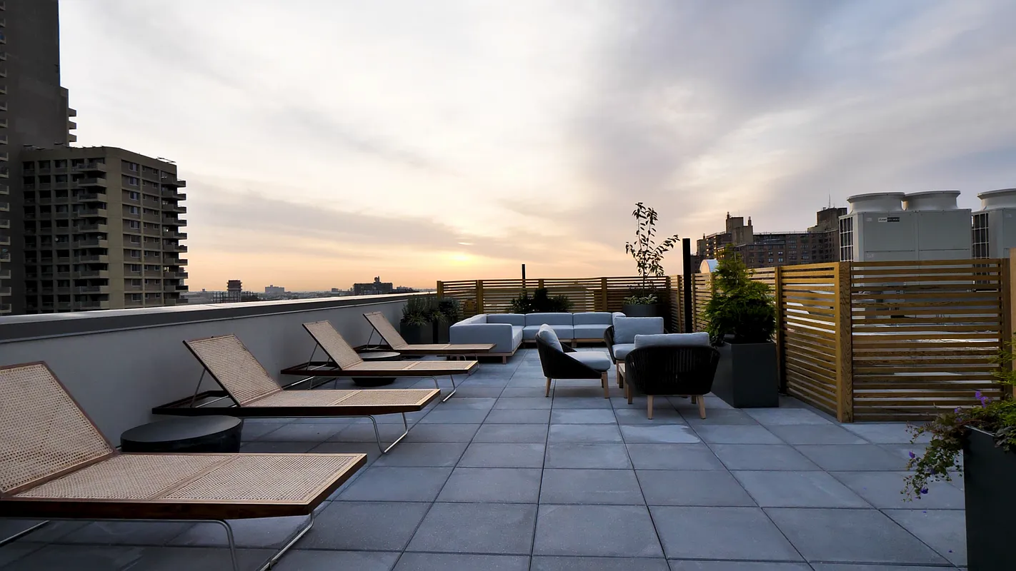 This image showcases a stylish rooftop terrace featuring modern outdoor furniture. The patio includes lounge chairs, a modular sofa, and stylish armchairs, all arranged on a tiled surface. A wooden privacy screen adds a touch of warmth and seclusion, while the city skyline provides a scenic backdrop, making it an ideal space for relaxation and entertaining.