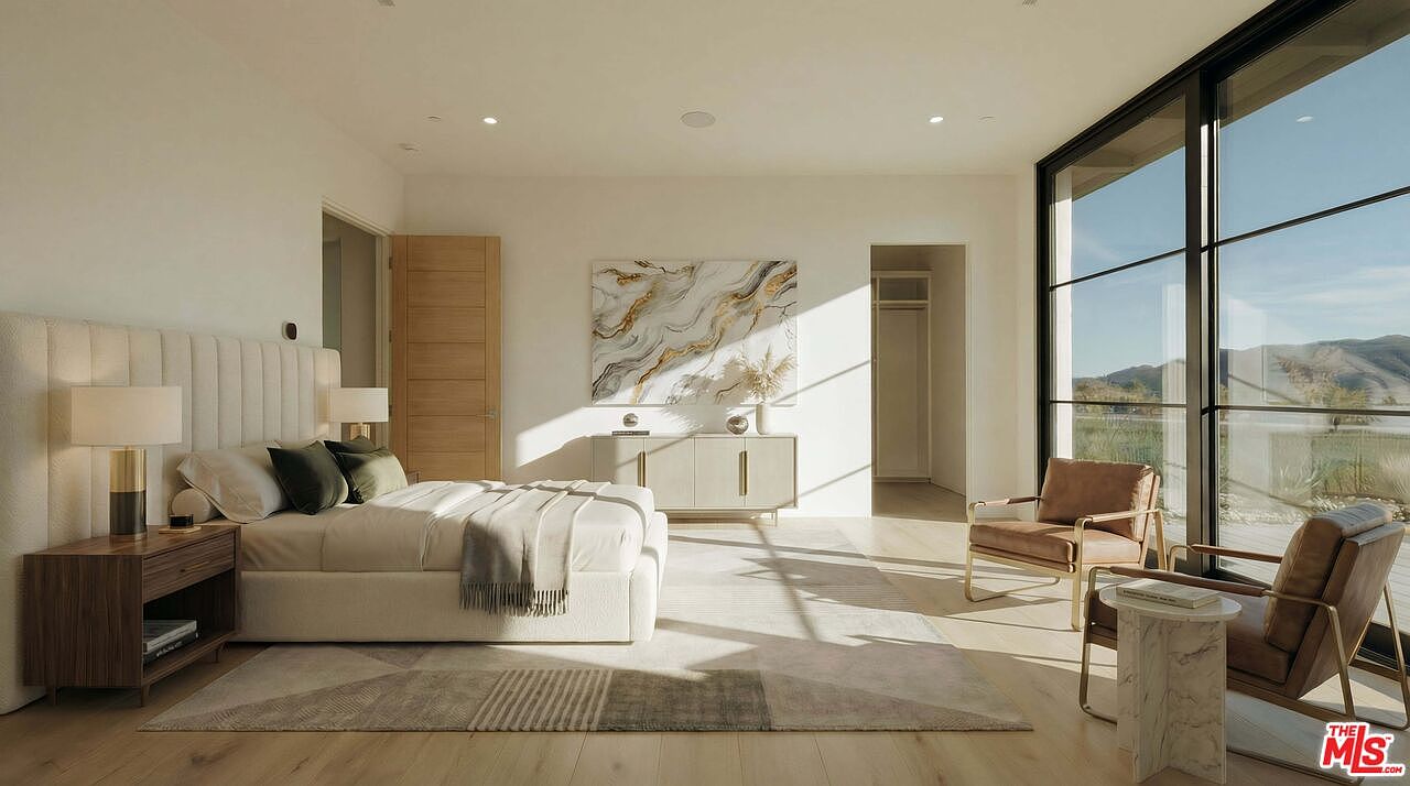 This spacious and serene primary bedroom features a neutral color palette, a plush upholstered headboard, and large floor-to-ceiling windows that flood the room with natural light. The minimalist design is complemented by a modern credenza, a textured area rug, and a cozy seating area, creating an atmosphere of sophisticated luxury. The perspective captures the entire room, highlighting the seamless blend of indoor comfort and the expansive outdoor view.