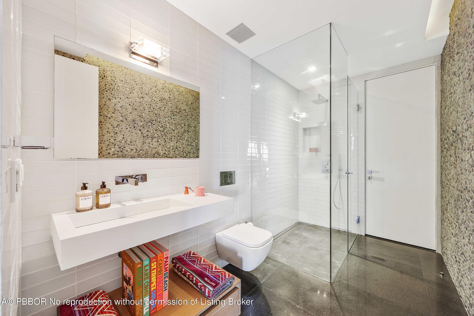 This is a modern primary bathroom featuring a floating vanity with a rectangular sink, complemented by sleek chrome fixtures and minimalist decor. The shower is enclosed with frameless glass, and the walls are tiled in a clean, horizontal pattern. A unique accent wall with pebble-like texture adds visual interest, and the overall design is contemporary and luxurious.