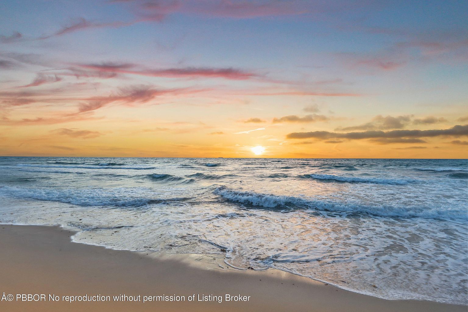 The image showcases a serene beach scene at sunset, with gentle waves rolling onto the sandy shore. The sky is painted with hues of orange, pink, and blue, creating a warm and inviting atmosphere. The overall impression is one of tranquility and natural beauty, perfect for highlighting the coastal lifestyle associated with the property.
