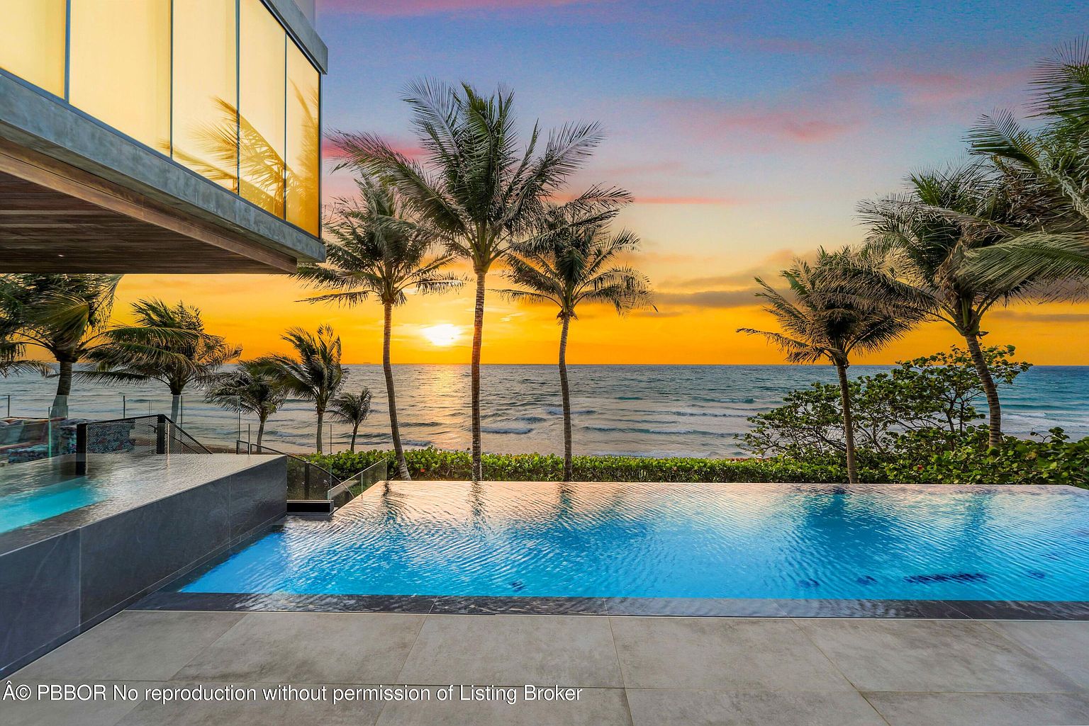 This image showcases a luxurious infinity pool overlooking the ocean at sunset. Palm trees frame the view, enhancing the tropical ambiance. The pool's design seamlessly blends with the horizon, creating a serene and inviting outdoor space perfect for relaxation and entertainment.