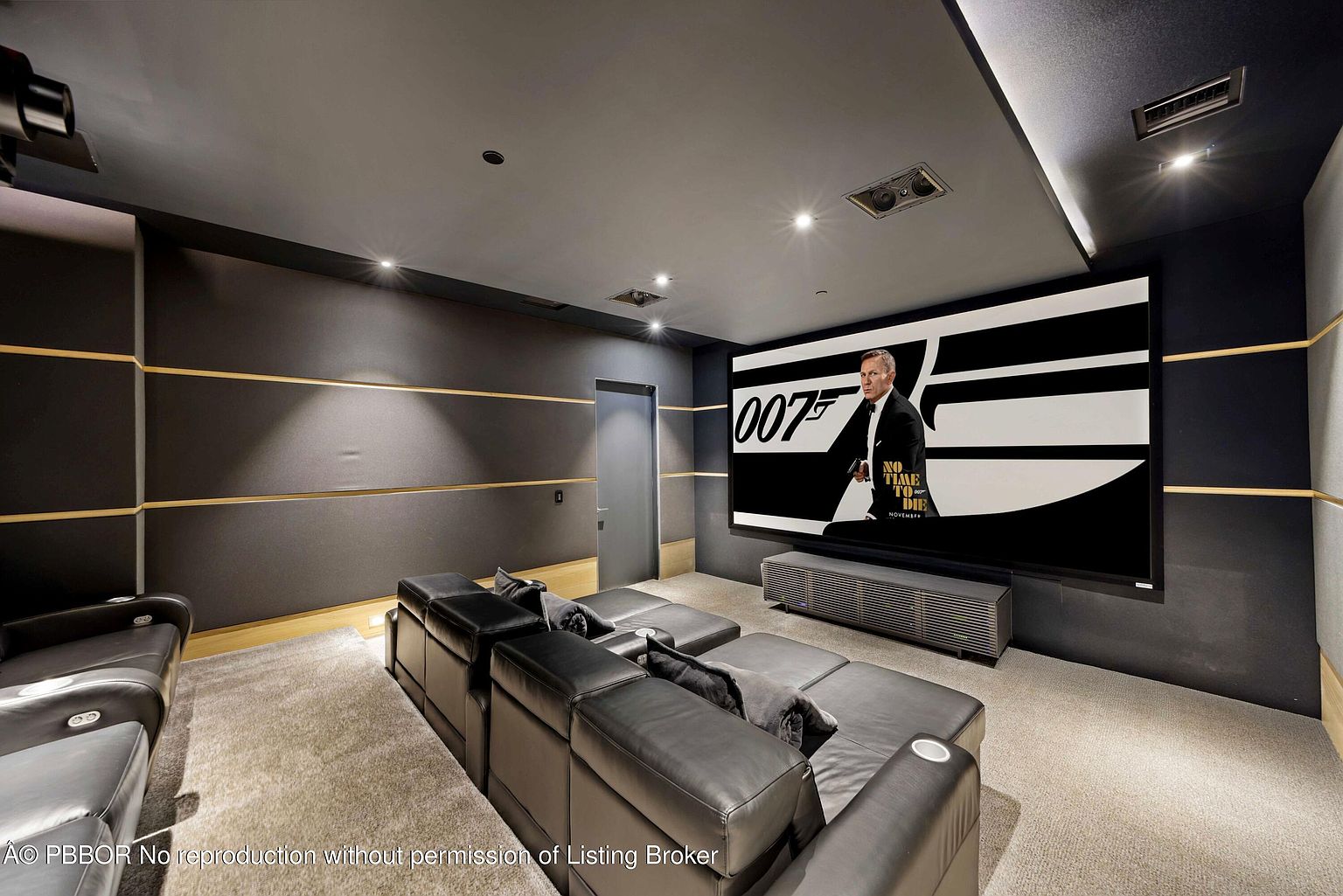 This is a luxurious home theater featuring tiered seating with plush black leather recliners, creating a comfortable and immersive viewing experience. A large screen displays a movie poster, and the room is designed with dark walls and strategic lighting to enhance the cinematic atmosphere. The overall impression is one of high-end entertainment and relaxation.