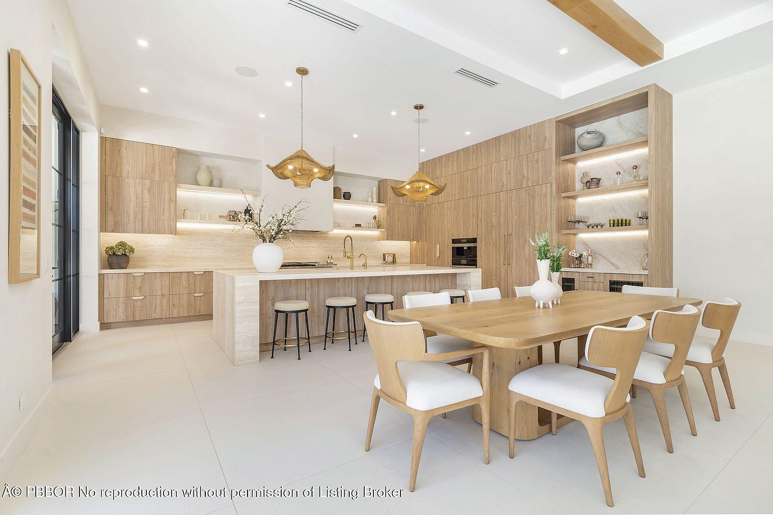 This interior shot showcases a modern, open-concept kitchen and dining area. The kitchen features light wood cabinetry, a large island with seating, and stylish pendant lighting. The dining area includes a wooden table with white upholstered chairs, complemented by built-in shelving and cabinetry, creating a cohesive and inviting space.