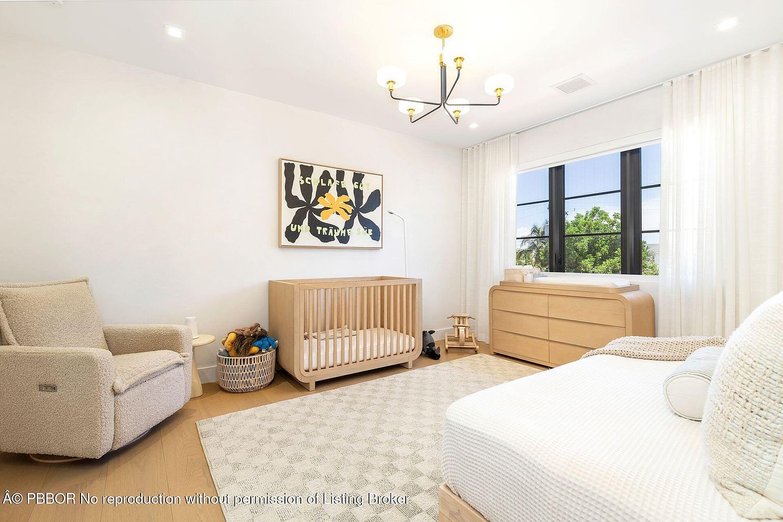 This is a bright and airy nursery featuring a light wood crib, a comfortable armchair, and a changing table/dresser combination. The room is decorated with a modern art piece and a neutral-toned rug, creating a calming and stylish environment. Natural light floods the space through a window dressed with sheer white curtains.