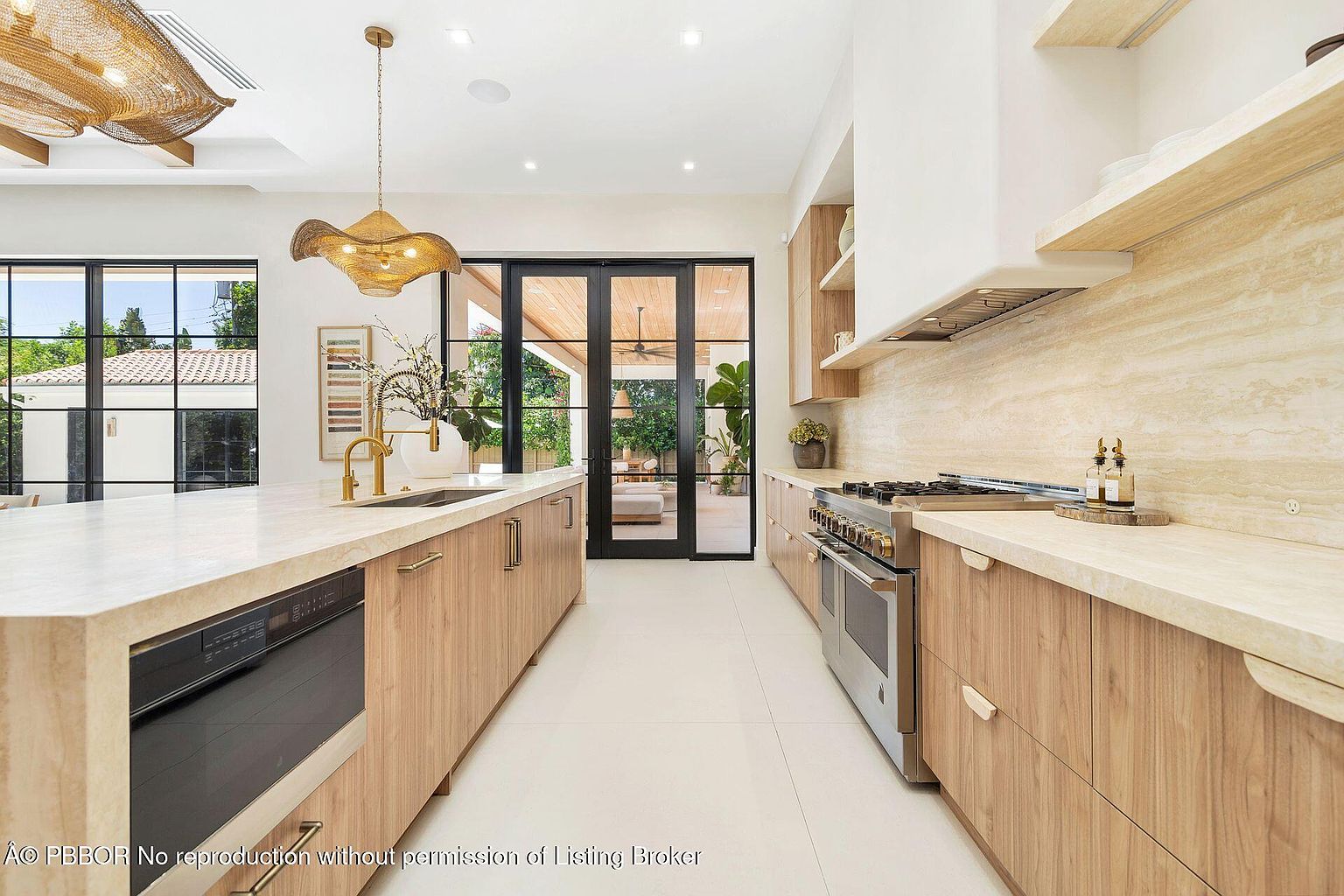 This is a bright and modern kitchen featuring light wood cabinetry, a large island with a marble countertop, and stainless steel appliances. The kitchen has a clean and minimalist design, with a focus on natural light and open space. Large glass doors lead to an outdoor patio area, enhancing the indoor-outdoor flow.