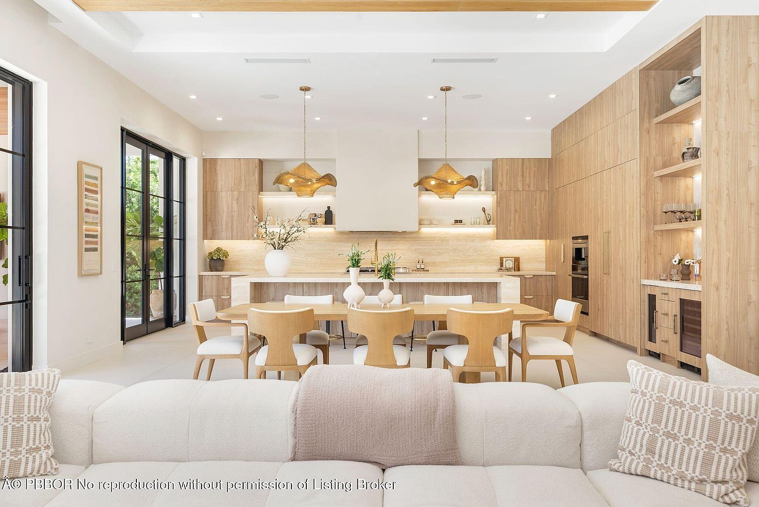 This is a bright and airy open-concept kitchen and dining area, featuring light wood cabinetry, a large dining table with modern chairs, and stylish pendant lighting. The kitchen boasts a clean, minimalist design with a focus on natural materials and a seamless flow into the living space, creating an inviting and sophisticated atmosphere. The view is from the living room looking into the kitchen and dining area.
