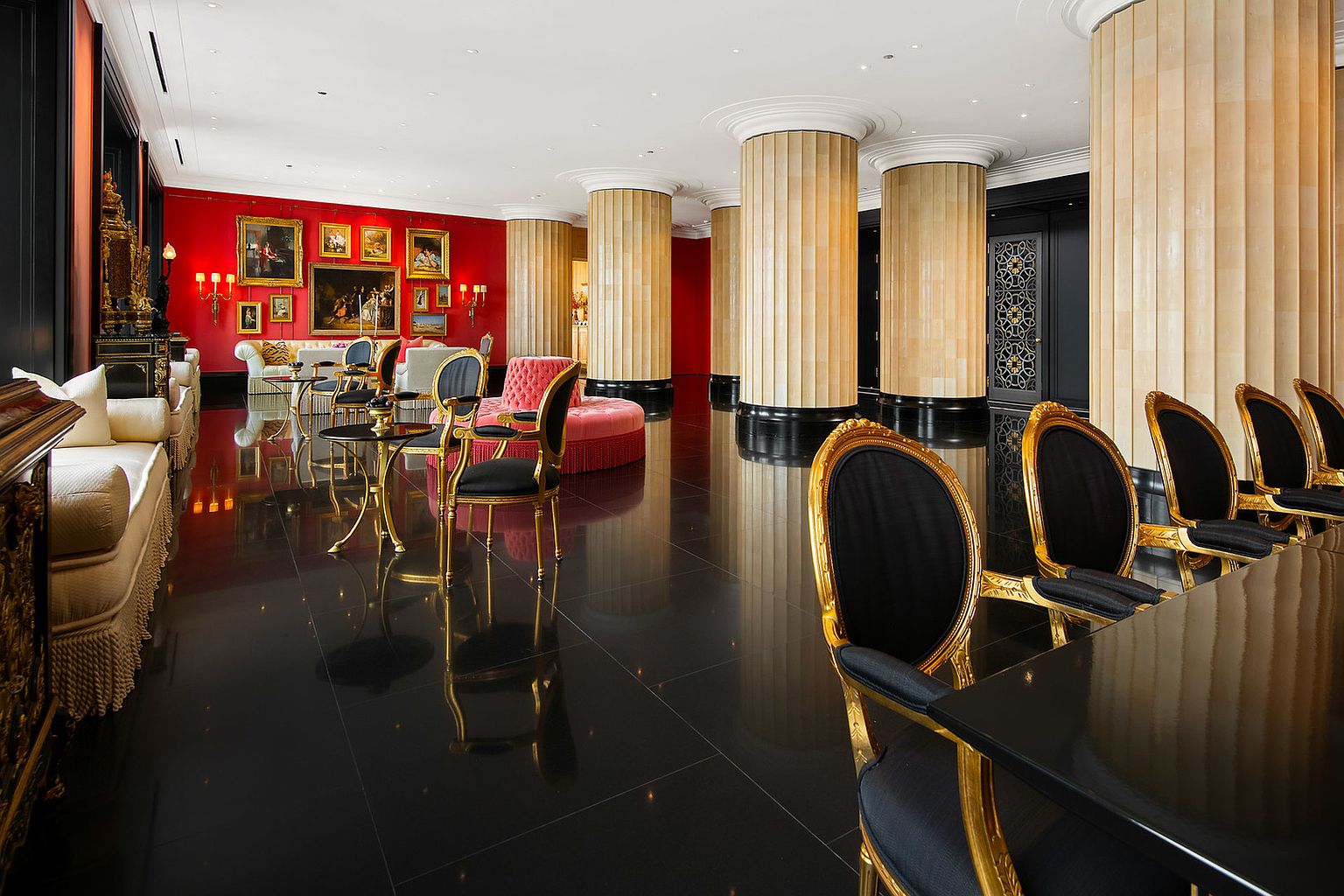 This opulent living room features a striking red accent wall adorned with classic paintings, complemented by elegant seating arrangements including plush sofas and ornate chairs with gold accents. The room is punctuated by grand, fluted columns and a glossy black tiled floor that reflects the ambient light, creating a luxurious and sophisticated atmosphere. The perspective is from a low angle, emphasizing the height and grandeur of the space.