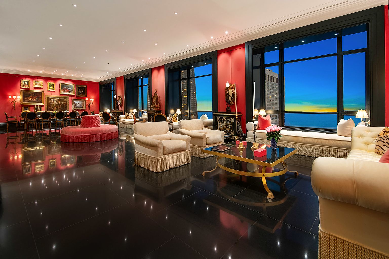 This is a luxurious living room featuring a glossy black tile floor, red accent walls, and large windows offering a stunning city and water view. The room is furnished with elegant seating arrangements, including plush armchairs and a long sofa, complemented by a gold-accented coffee table. The perspective is wide-angle, showcasing the room's spaciousness and high-end design.
