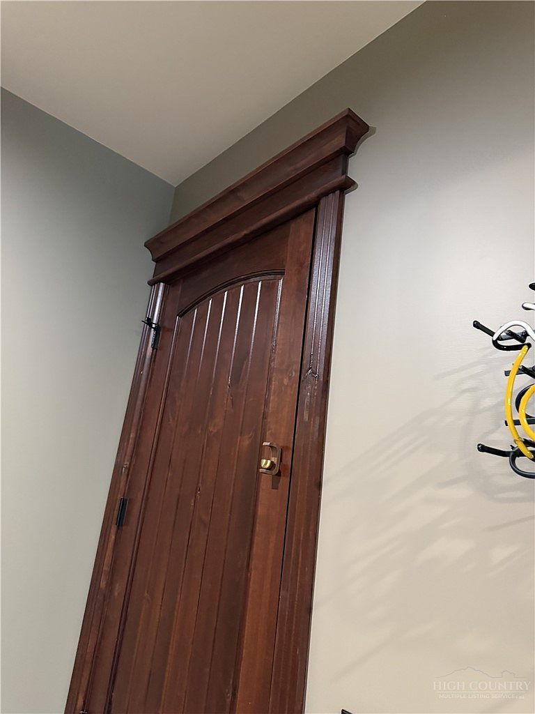 This image captures a close-up, low-angle perspective of a dark-stained wood door featuring a classic arched top and vertical paneling. The door is framed by ornate, heavy wood trim with a prominent crown molding header, adding a traditional and sophisticated architectural detail to the room. To the right, a portion of a decorative yellow metal wall rack is visible against the neutral-toned wall.