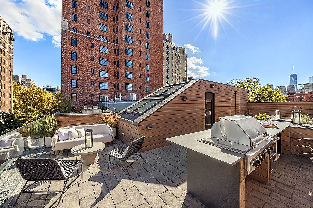 This image showcases a luxurious rooftop patio/deck area, complete with modern outdoor furniture, including a sleek sofa and stylish chairs. A built-in outdoor kitchen with a stainless steel grill adds a touch of sophistication, while the surrounding cityscape provides a stunning backdrop. The space is designed for relaxation and entertainment, offering a premium outdoor living experience.