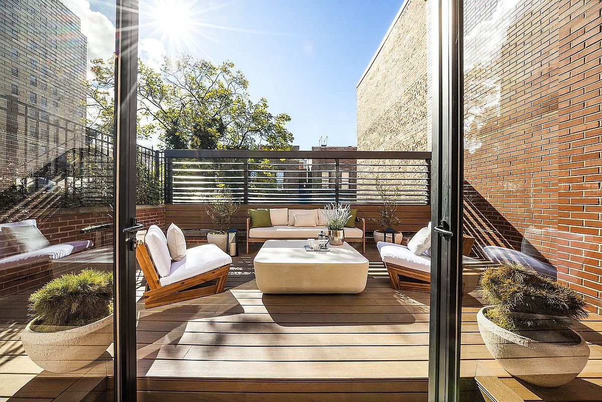 This image showcases a stylish and inviting outdoor patio or deck area. The space features modern furniture, including a sofa, chairs, and a coffee table, all arranged on a wooden deck. A sleek black fence provides privacy, while potted plants add a touch of greenery, creating a relaxing and sophisticated outdoor living space.