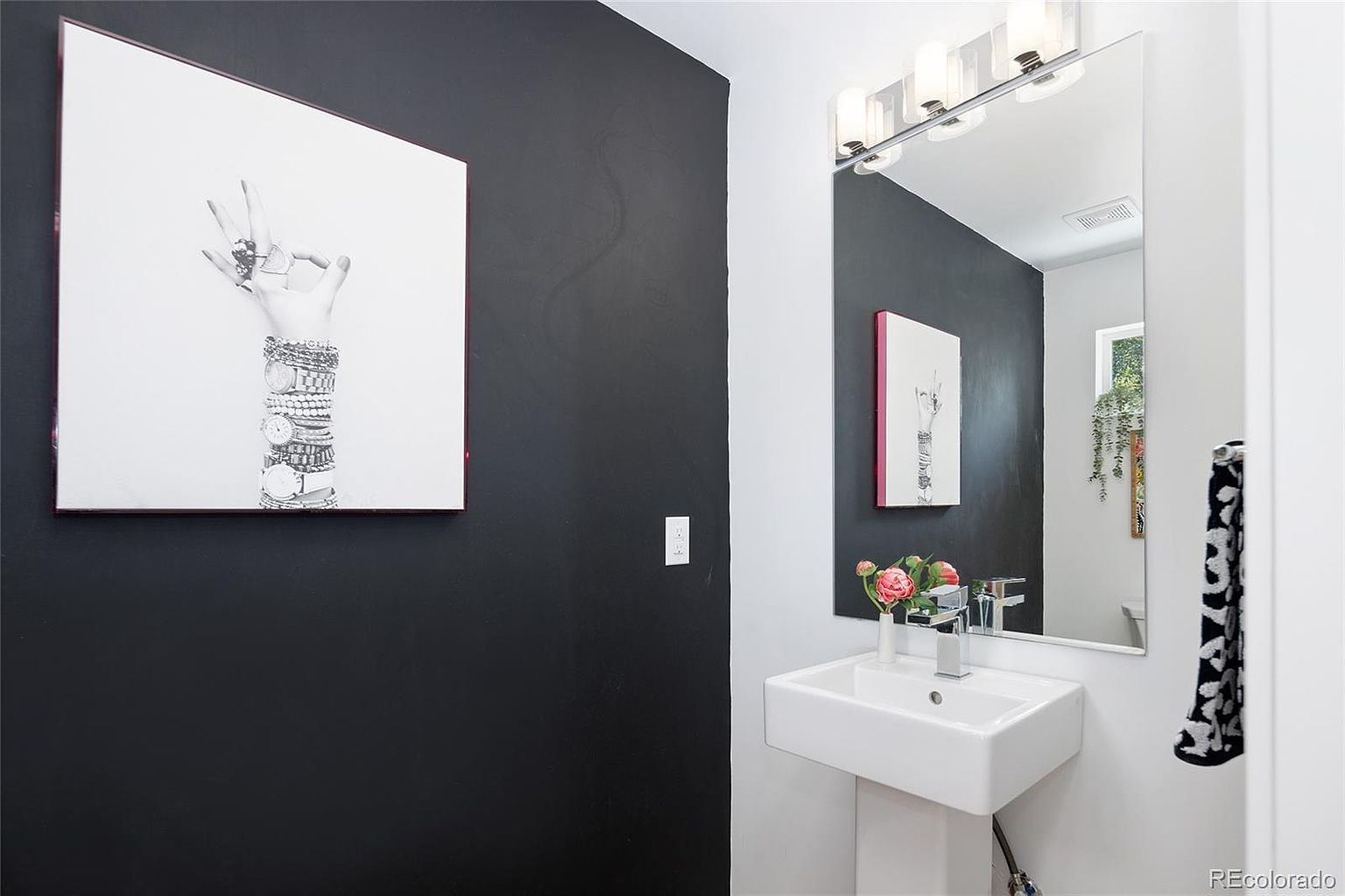 This is a modern guest bathroom featuring a sleek, wall-mounted sink with a chrome faucet. The walls are painted in a contrasting black and white scheme, with a framed art piece adding a touch of personality. A large mirror reflects the space, enhancing the sense of openness and light.
