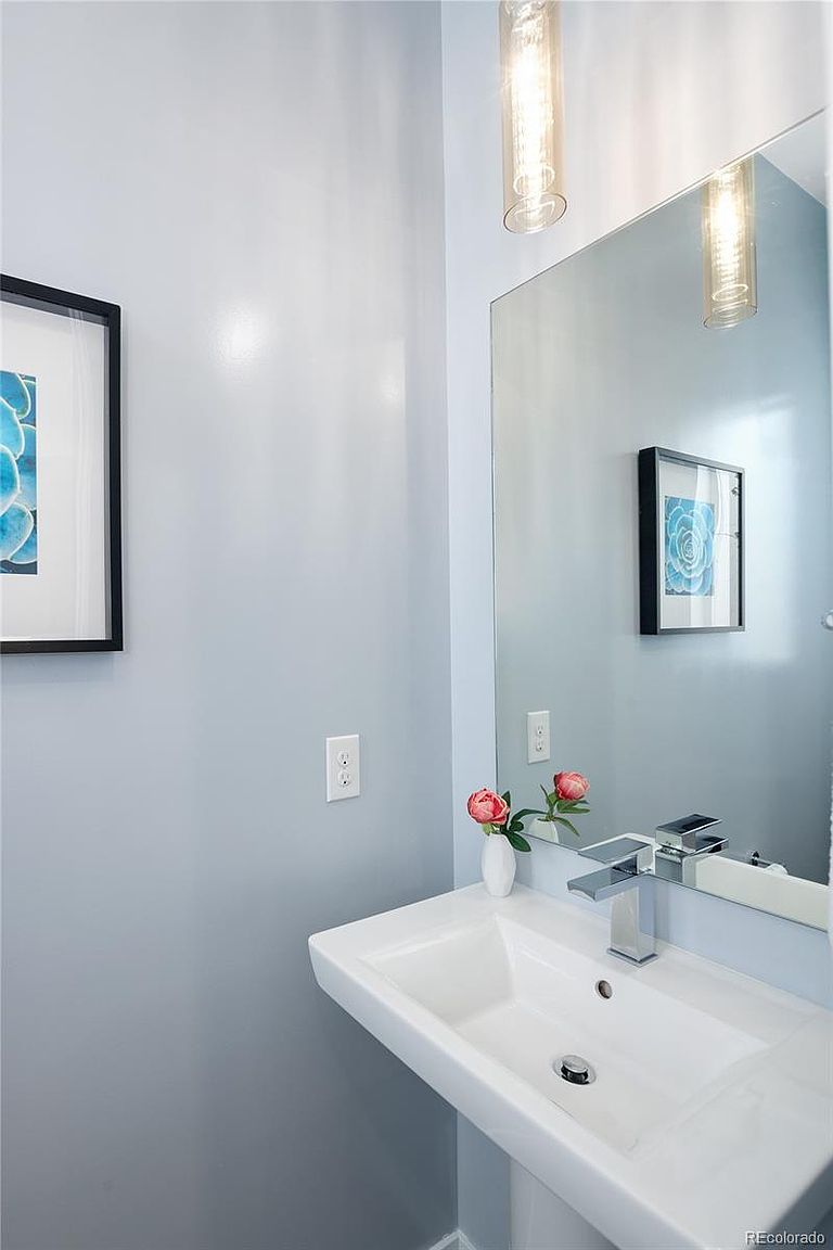 This is a well-lit guest bathroom featuring a modern, wall-mounted sink with a chrome faucet. A large mirror reflects the light and a framed artwork, enhancing the sense of space. The walls are painted in a soft blue-gray, creating a serene and clean atmosphere.