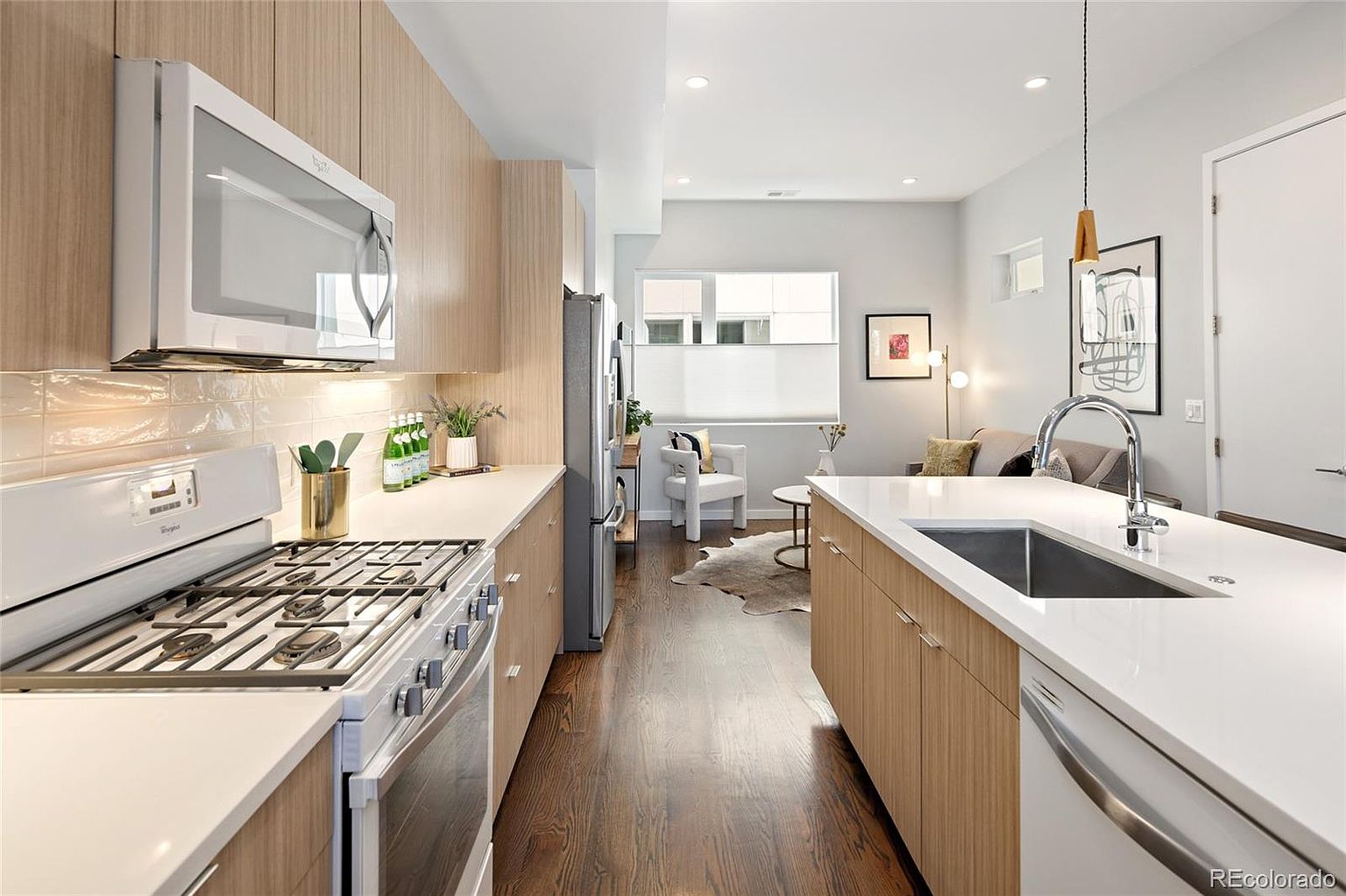 This is a bright and modern kitchen featuring light wood cabinetry and white countertops. Stainless steel appliances, including a gas range and microwave, add a sleek touch. The open layout connects to a living area, creating a spacious and inviting atmosphere.